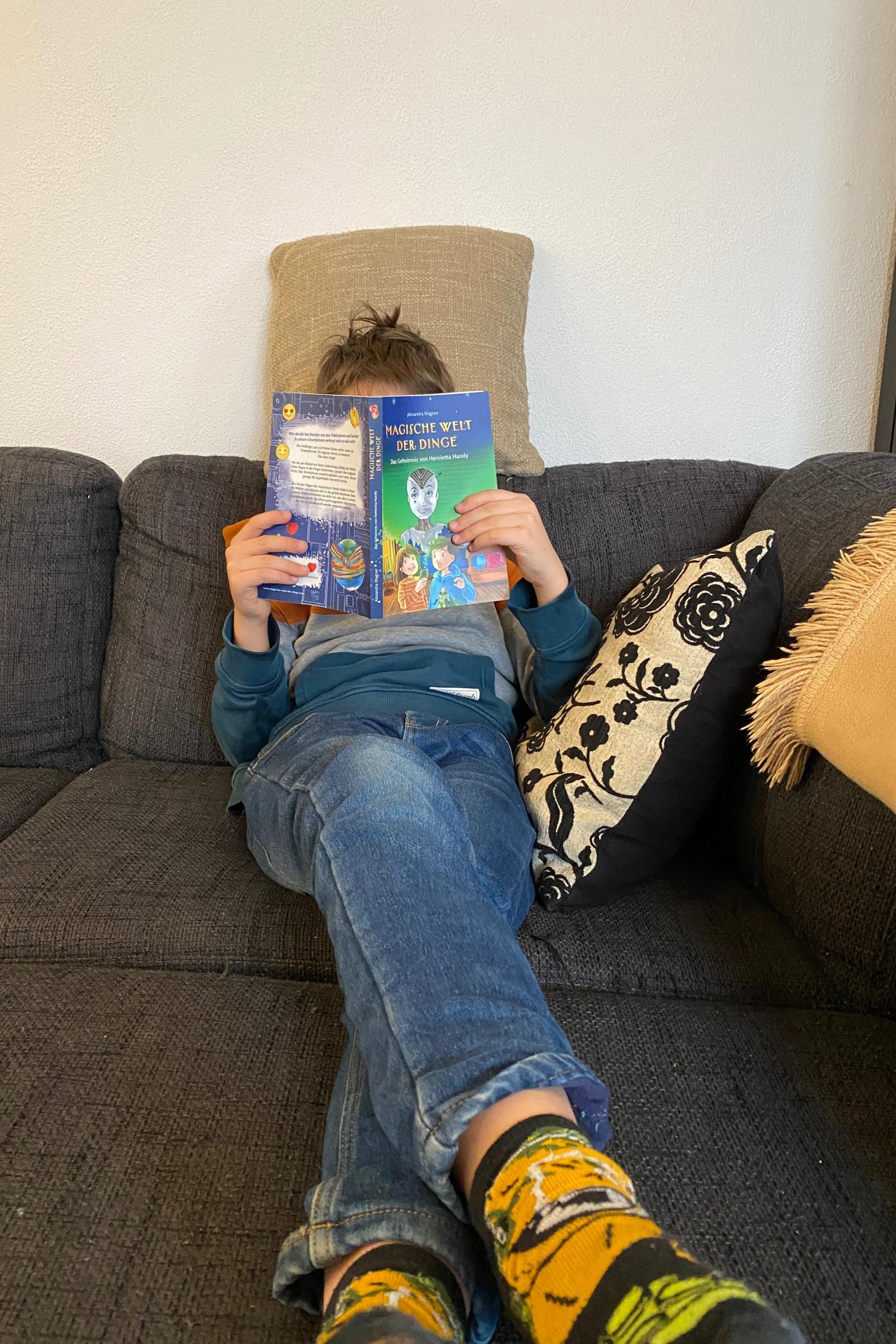 Junge liest das Buch Das geheimes von Henrietta Handy auf der Couch sitzend