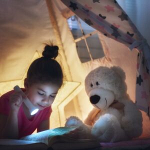 Mädchen liest mit Taschenlampe im Indoorzelt ein Buch