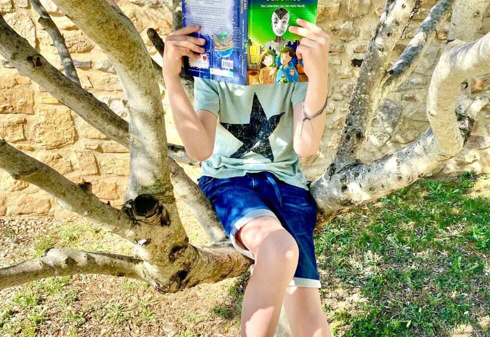 Junge liest mit Buch vor Gesicht, während er im Baum sitzt