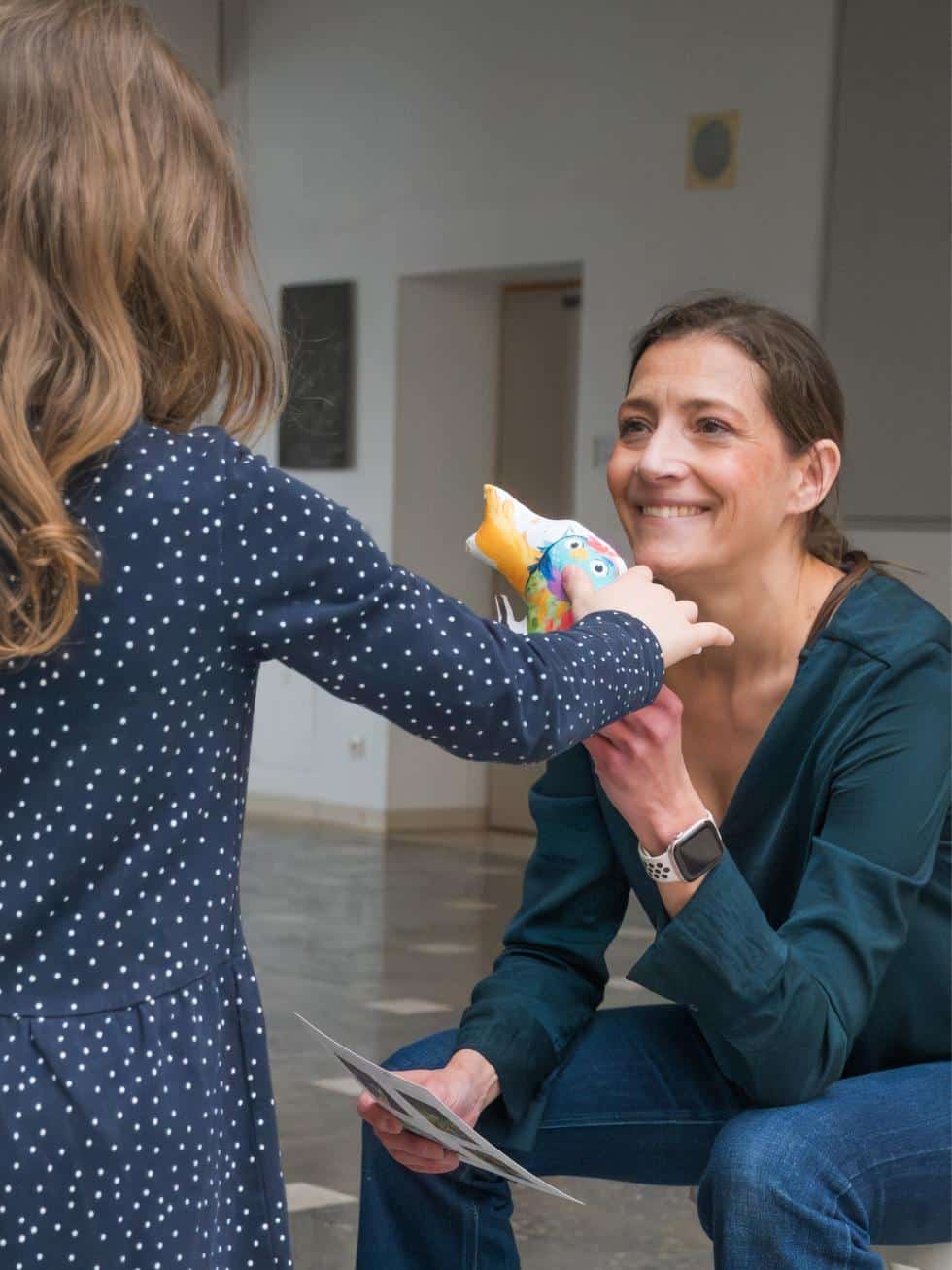 Mädchen streichelt Stofftier Eule Ada, das ihm Alexandra Wagner lächelnd hinhält