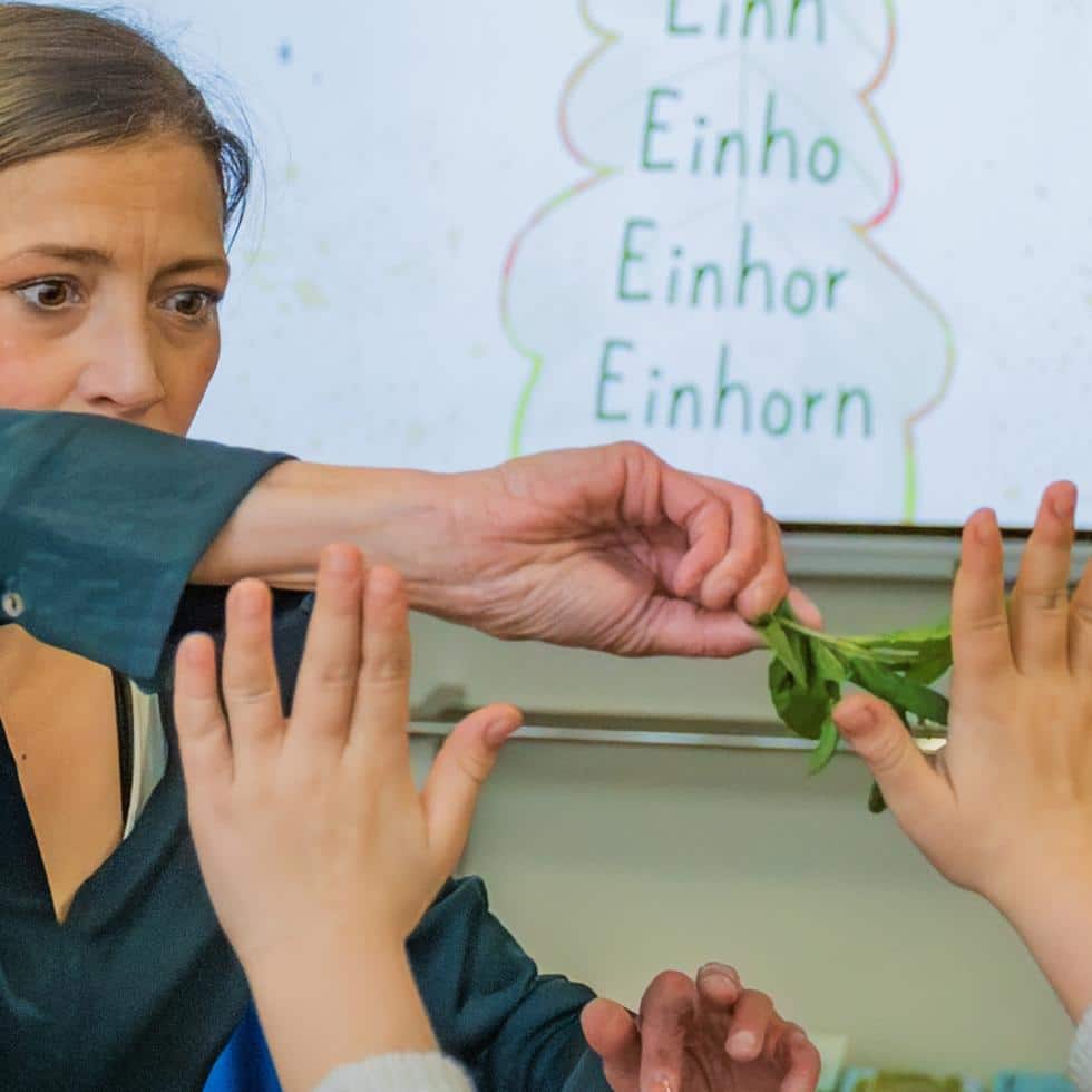 Alexandra Wagner streift ein Büschel Minze über die Hände von Kindern