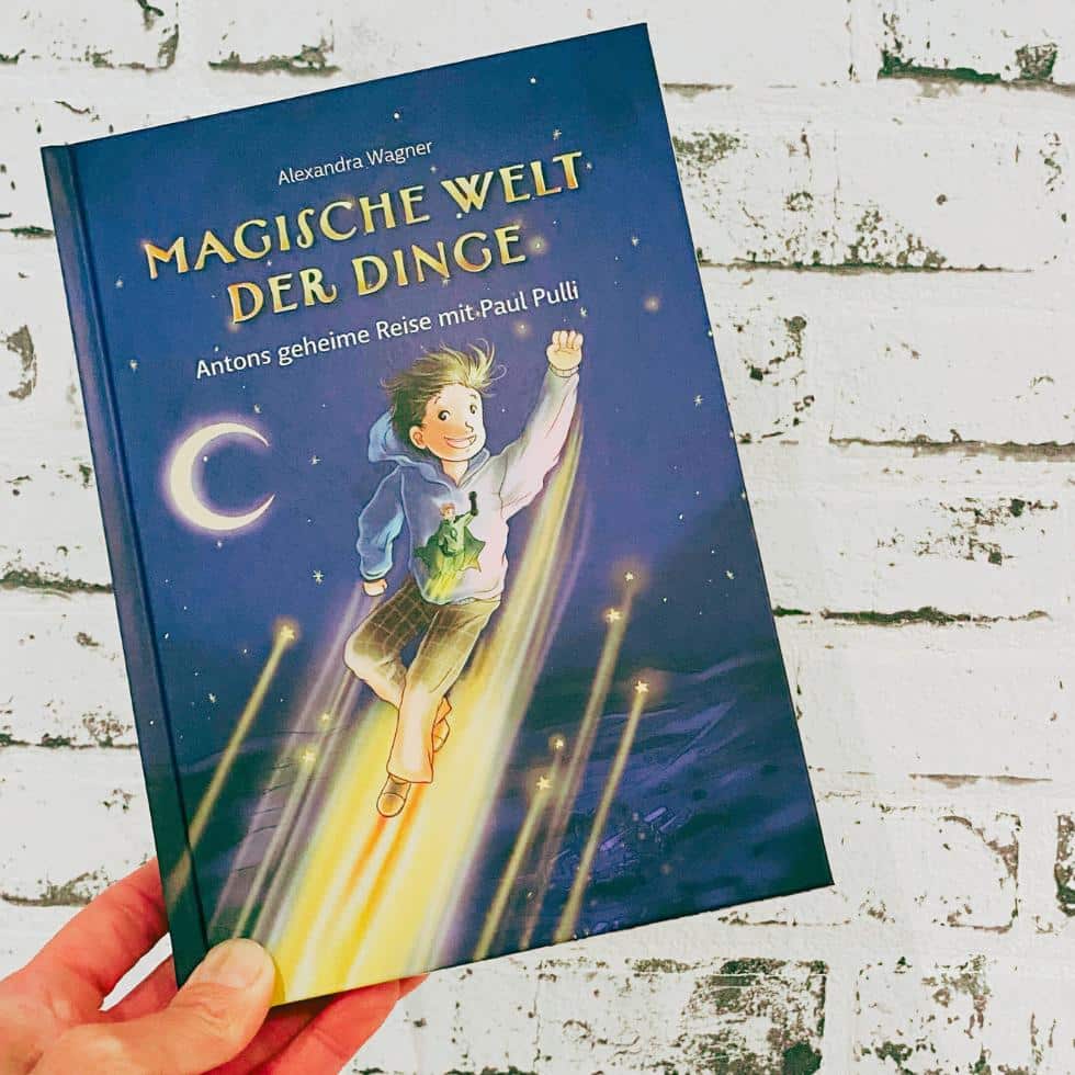 Hand hält Kinderbuch Magische Welt der Dinge, Antons geheime Reise mit Paul Pulli hoch