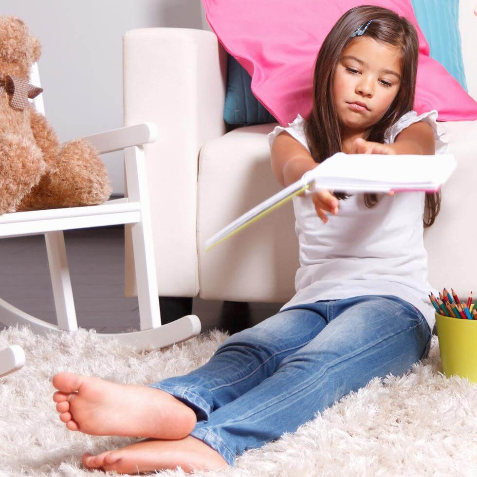 Mädchen im Grundschulalter sitzt in Kinderzimmer und wirft Buch mit genervtem Gesichtsausdruck weg