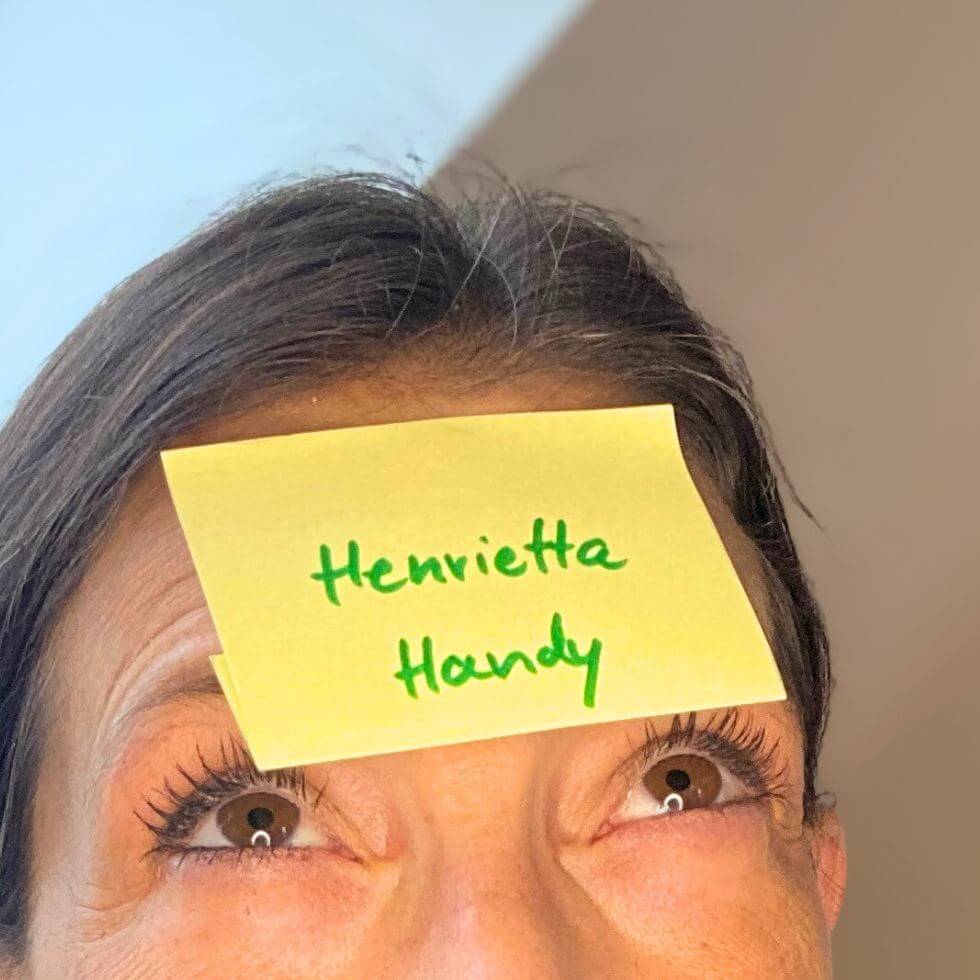 Nahaufnahme eines Zettels, auf dem Henrietta Handy steht, der auf der Stirn einer Frau klebt
