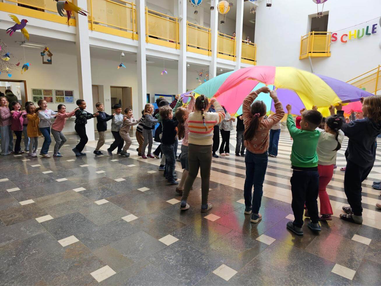 Kinder stehen in Schlange und laufen unter einem regenbogenfarbenem Schwungtuch hindurch