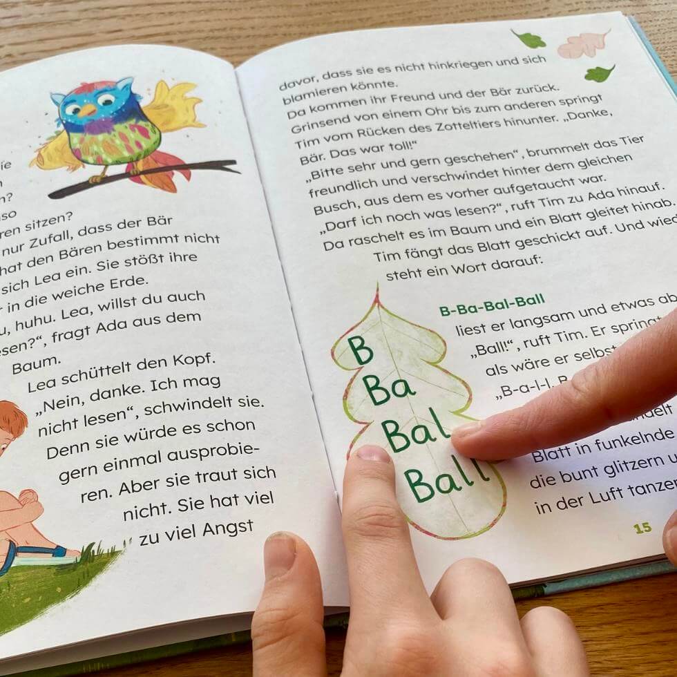 lesetandem-treppenwort Aufgeschlagenes Buch "Lesewald" mit Treppenwort "Ball", Finger von Mutter und Sohn zeigen darauf