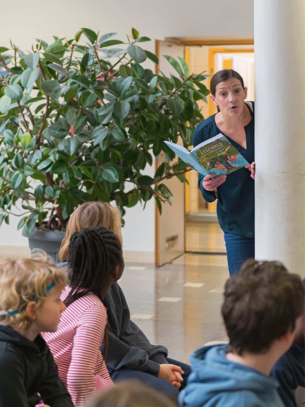 Alexandra Wagner lugt lesend hinter einer Säule hervor.