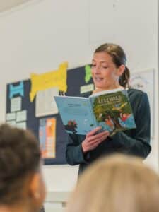 Alexandra Wagner liest Kindern aus ‚LESEWALD: Der Zauber erwacht‘ vor; Publikum im Vordergrund.