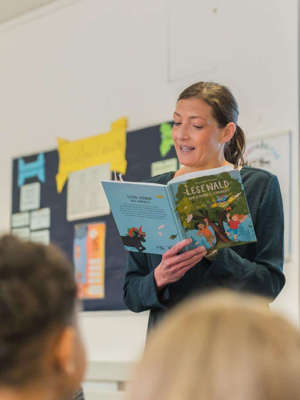 Alexandra Wagner liest Kindern aus ‚LESEWALD: Der Zauber erwacht‘ vor; Publikum im Vordergrund.